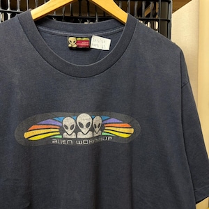 May include: A dark navy blue short-sleeve t-shirt featuring a graphic of three grey alien heads centered within a black oval surrounded by a rainbow-colored arc. The text ALIEN WORKSHOP is printed below the aliens. A tag shows 23.5/30.