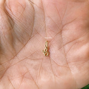 May include: A small, gold-colored pendant in the shape of the letter "C". The pendant is suspended from a small loop at the top. The pendant is displayed against a blurred background.