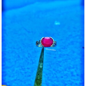 Op de afbeelding: Een zilveren ring met een grote, ovaalvormige, helderrode edelsteen. De ring heeft decoratieve filigraan details aan de zijkanten. De tekst "Mita jewellers" is zichtbaar eronder.