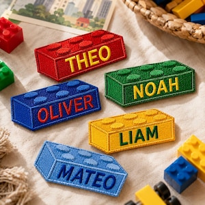 May include: Five rectangular embroidered patches shaped like building blocks in red, green, blue, yellow, and light blue. Each patch features a name stitched in a contrasting color: THEO, NOAH, OLIVER, LIAM, and MATEO, with raised circular studs on top.