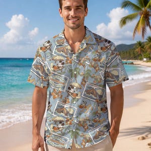 Może przedstawiać: Jasnoniebieska koszula z krótkim rękawem z tropikalnym nadrukiem przedstawiającym Myszka Miki, palmy i napis "Polynesian Resort". Koszula ma luźny krój, idealna na wakacje lub do noszenia na co dzień.