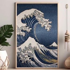 May include: A framed print of a Japanese wave art piece. The artwork features a large wave with white crests against a dark blue background. The print is displayed on a wooden surface, with plants and decorative items in the foreground.