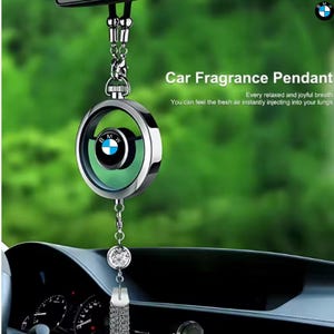 Puede incluir: Un colgante de fragancia para coche con un marco circular plateado y un logotipo de BMW. El colgante cuelga de una cadena y presenta un cristal decorativo y una borla. El texto en la imagen dice "Car Fragrance Pendant".