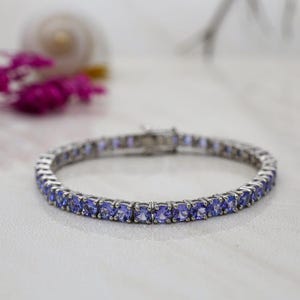 Può includere: Un bracciale tennis color argento caratterizzato da una fila continua di pietre preziose taglio rotondo color viola chiaro, incastonate in singole griffe metalliche. Il bracciale è dotato di una chiusura in metallo e un design uniforme.