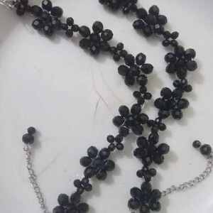 Puede incluir: Juego de joyas de cuentas negras con collar y pulsera. El collar y la pulsera est&aacute;n adornados con cuentas en forma de flor y conectados por una cadena y un cierre plateados. Las cuentas tienen un dise&ntilde;o facetado.