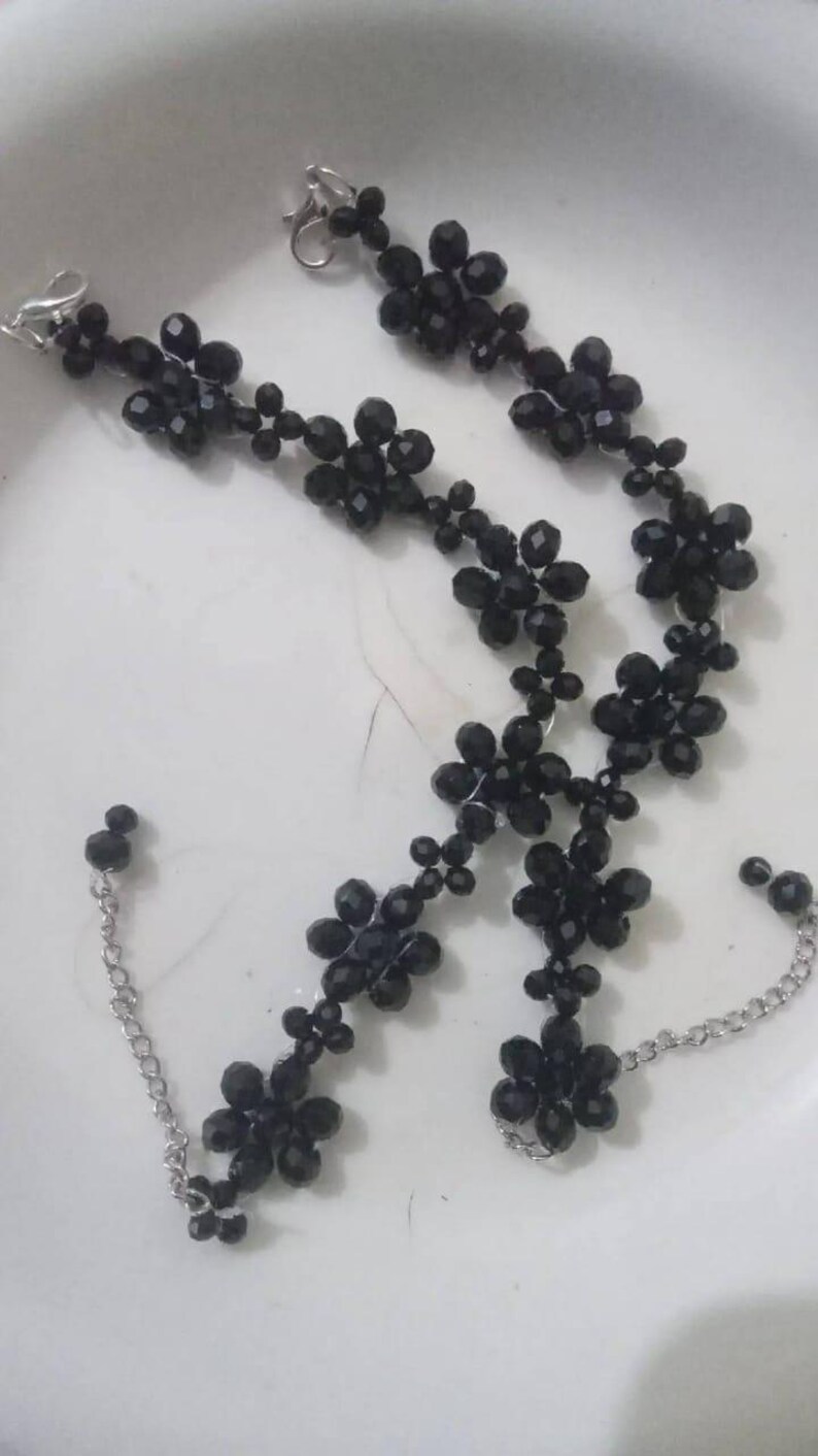 Puede incluir: Juego de joyas de cuentas negras con collar y pulsera. El collar y la pulsera est&aacute;n adornados con cuentas en forma de flor y conectados por una cadena y un cierre plateados. Las cuentas tienen un dise&ntilde;o facetado.