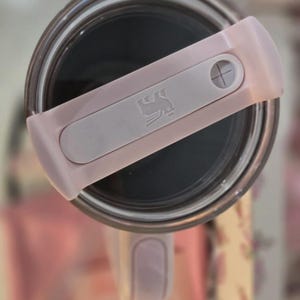 May include: A white ceramic mug with a black handle and the text "But First, Coffee" in a black, bold font. The mug is sitting on a wooden surface. The mug is 4 inches tall.