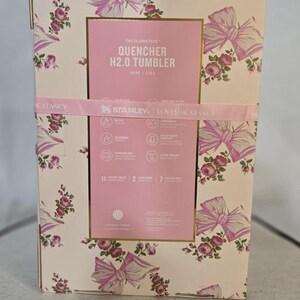 May include: A white ceramic mug with a black handle and the text "But First, Coffee" in a bold, black font. The mug is set against a blurred background, suggesting a cozy setting.