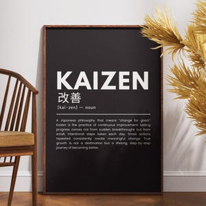 Puede incluir: Impresión enmarcada en blanco y negro con la palabra "KAIZEN" en letras blancas grandes. La impresión también incluye caracteres japoneses y una definición. Una silla de madera y plantas secas decorativas en el fondo.