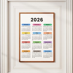 May include: A framed 2026 calendar with a brown wooden frame. The calendar features a white background with the year 2026 at the top. Each month is color-coded with a different color, and the days of the week are listed.