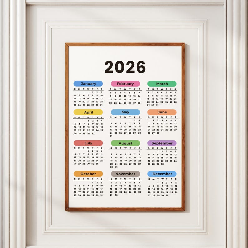 May include: A framed 2026 calendar with a brown wooden frame. The calendar features a white background with the year 2026 at the top. Each month is color-coded with a different color, and the days of the week are listed.