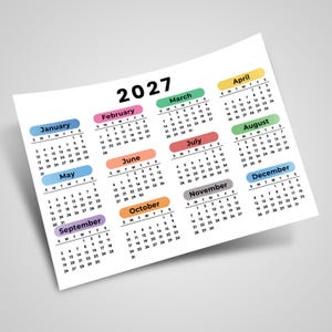 Könnte beinhalten: Ein Jahreskalender für 2027 auf einem weißen Blatt, der zwölf Monatsübersichten in Reihen angeordnet zeigt. Jeder Monatsname steht in einem farbigen, abgerundeten Rechteck, darunter sind die Wochentage und Daten aufgelistet.