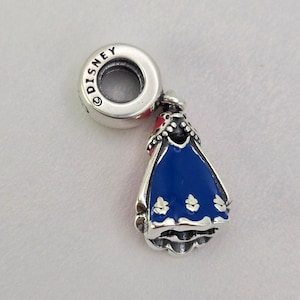May include: A silver charm with a blue and red enamel design. The charm features a stylized dress shape with a Disney logo on the top. The dress has a blue bodice and a red collar.