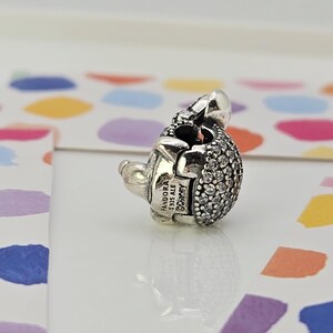 May include: A silver charm with a rounded, textured body encrusted with small, clear crystals. The charm has a small, smooth silver head and a clasp. The charm is stamped with "PANDORA S925 ALE &copy;Disney".