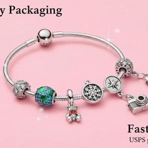 May include: A silver charm bracelet with various charms, including a globe, a camera, a book, a snowflake, and a teddy bear. The bracelet is on a pink background. The text "Gift-Ready Packaging" is at the top.
