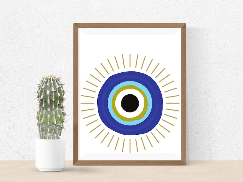May include: A framed print featuring a stylized eye design. The eye is composed of concentric circles in blue, gold, and black, surrounded by gold rays. A cactus in a white pot is to the left of the framed art.