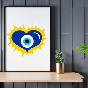 May include: A framed art print featuring a blue heart with an eye design, set against a yellow burst. The artwork is displayed on a light wood shelf with a small potted plant and a gold-colored pot. The background is a dark gray wall.