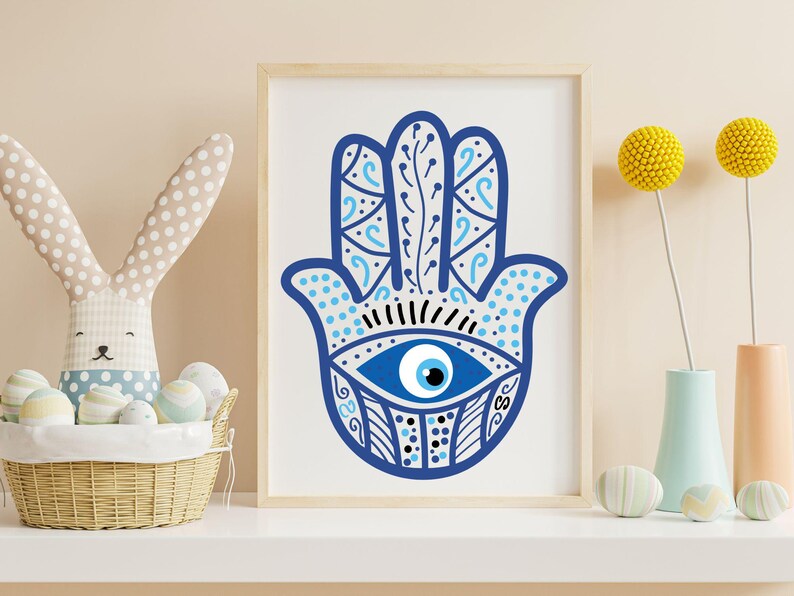 May include: A framed print featuring a blue Hamsa hand design with an eye in the center. The hand is decorated with intricate patterns and details. The artwork is displayed on a white surface, with a basket, decorative eggs, and flowers in the background.