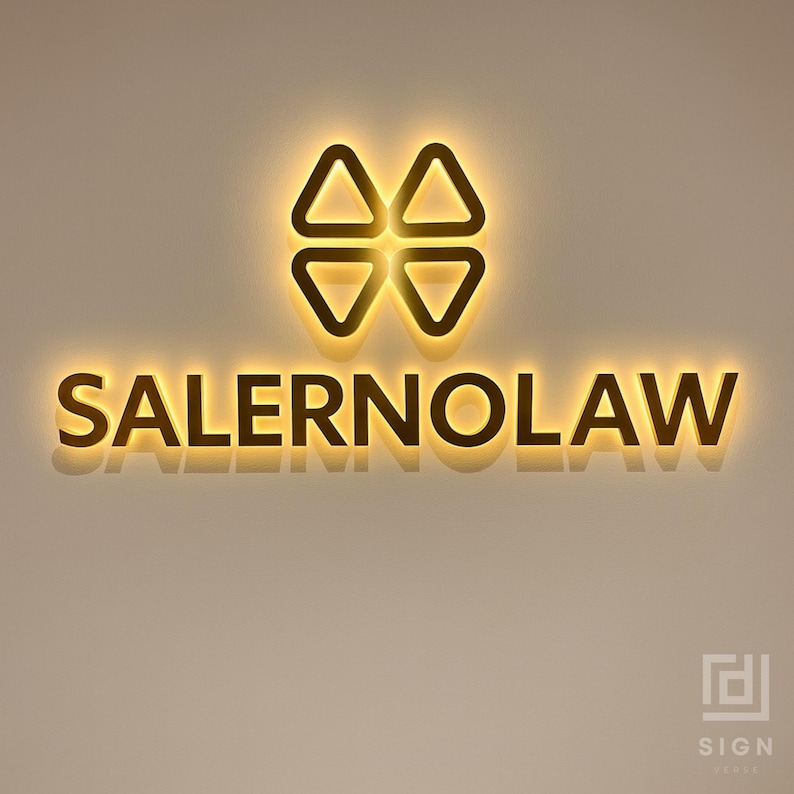 May include: Illuminated sign for Salerno Law. The sign features a four-part geometric logo above the business name. The text "SALERNOLAW" is in a bold, sans-serif font. The sign has a warm, golden glow against a neutral wall.