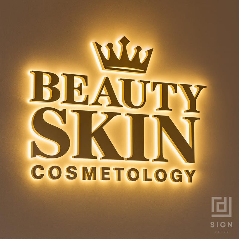 May include: Illuminated sign for a beauty and skin care business. The sign features the words "BEAUTY SKIN COSMETOLOGY" in a gold color, with a crown above the text. The sign is lit with a warm, yellow glow.