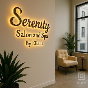 May include: Illuminated sign for "Serenity Salon and Spa By Eliana" in a spa setting. The sign is gold with a warm glow, mounted on a neutral wall. A beige armchair, a small table, and a plant are in the background.