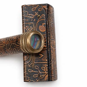 May include: A vintage brass and leather kaleidoscope with a decorative case. The kaleidoscope has a brass eyepiece and a brown leather body with embossed patterns. The case is also brown leather with similar embossed designs.