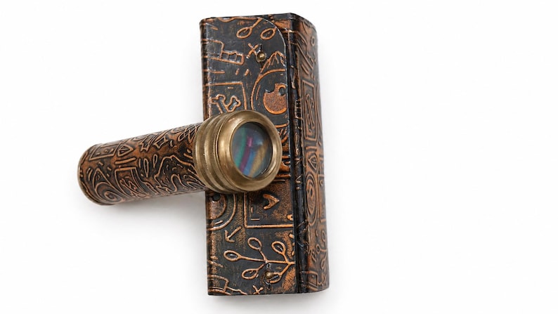 May include: A vintage brass and leather kaleidoscope with a decorative case. The kaleidoscope has a brass eyepiece and a brown leather body with embossed patterns. The case is also brown leather with similar embossed designs.