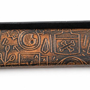 May include: A brown leather case with a black top, featuring embossed designs of knives, poison bottles, and other symbols. The case has a distressed, vintage look, with a dark brown and black color scheme.