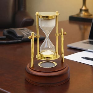 以下が含まれることがあります： 金色の金属フレームと木製のベースを備えた砂時計。 ガラス容器には白い砂が入っています。 砂時計は装飾的なデスクアクセサリーです。