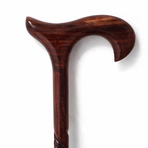 May include: A close-up of a wooden walking cane with a curved handle. The cane is a rich, dark brown color with a glossy finish. The handle is ergonomically designed for a comfortable grip. The shaft has a decorative, carved design.