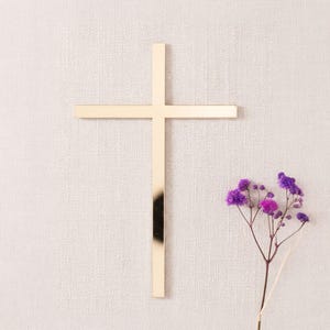 Schlichtes goldenes Kreuz als Dekoration für die Tortenseite, auf beigem Stoff neben einem Zweig mit kleinen violetten Blüten.