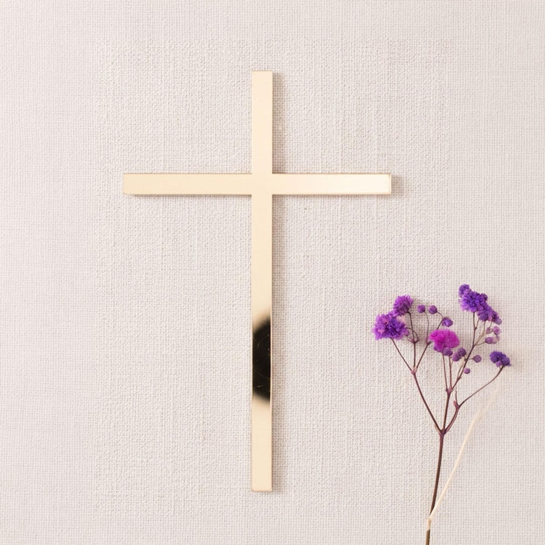 Schlichtes goldenes Kreuz als Dekoration für die Tortenseite, auf beigem Stoff neben einem Zweig mit kleinen violetten Blüten.