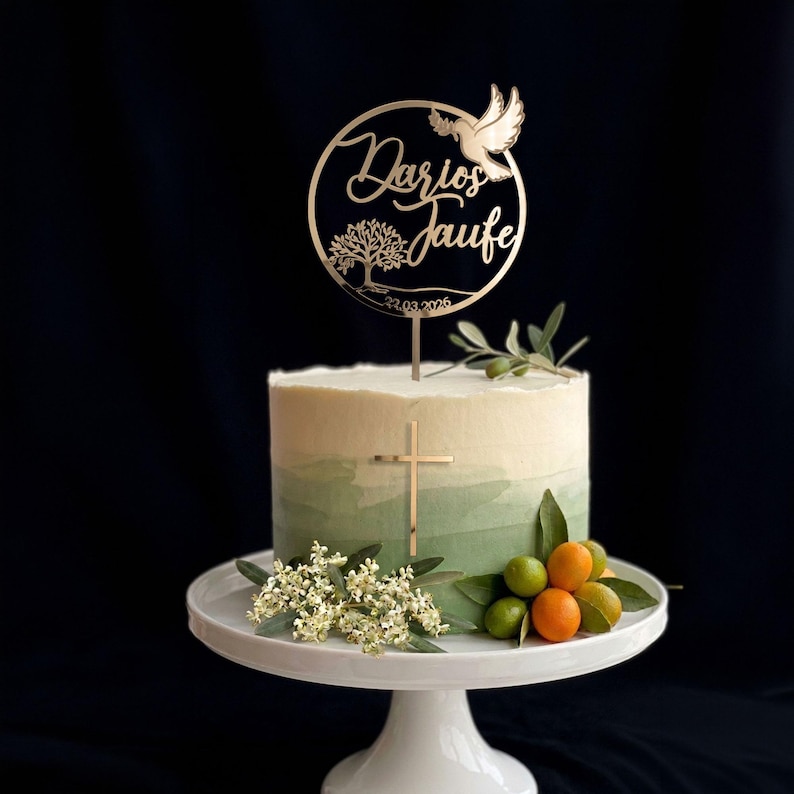 Tauftorte in Weiß und Grün mit rundem goldenem Cake Topper „Zur Taufe“, Taubenmotiv und floralen Details. Ein goldenes Kreuz schmückt die Tortenseite.