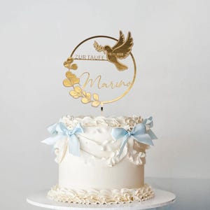 Cake Topper Taufe gold mit Namen „Marius“ und Schriftzug „Zur Taufe“ auf einer weißen Torte mit blauen Schleifen und goldfarbenen Details.