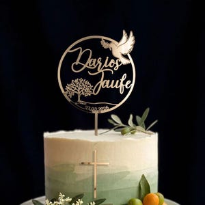Goldener Taufe-Cake-Topper mit Taube und rundem Rahmen auf einer weiß-grünen Torte mit goldenem Kreuz vor dunklem Hintergrund.