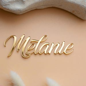 Personalisierter Namensschriftzug „Melanie“ aus goldfarbenem Spiegelacryl als Tortendeko zur Erstkommunion für Mädchen und Jungen.