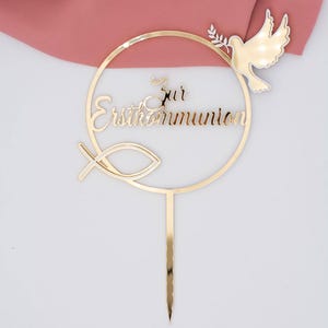 Detailansicht des goldenen Cake Toppers zur Erstkommunion aus Spiegelacryl mit filigranem Schriftzug, Fischsymbol und Taube als festlicher Tortenaufsatz.