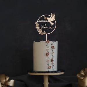 Runder Tortenaufsatz „Zur Taufe“ mit Namen Amelia und Taubenmotiv auf einer hohen weißen Torte mit Blütenverzierung – personalisierte Tortendeko zur Taufe.