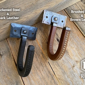Two metal and leather wrapped wall gun hooks. One features blackened steel and black leather, the other brushed steel and brown leather. Hutton Forge
