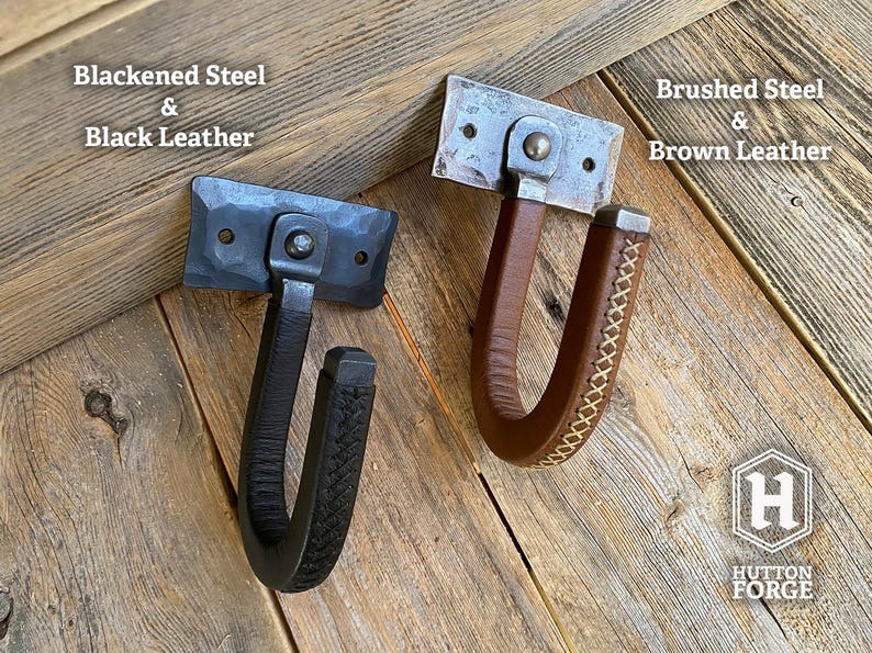 Two metal and leather wrapped wall gun hooks. One features blackened steel and black leather, the other brushed steel and brown leather. Hutton Forge