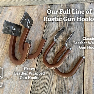 Rustic gun hooks with brown leather wrapping and metal hardware. The image displays two styles: "Heavy Leather Wrapped Gun Hooks" and "Classic Leather Wrapped Gun Hooks". The text "Our Full Line of Rustic Gun Hooks" is also visible.