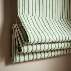 May include: A close-up of a green and white striped Roman blind. The fabric is folded in horizontal layers, displaying the pattern. The green stripes are evenly spaced against a white background, creating a clean, classic appearance.