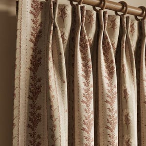 May include: Cream and burgundy patterned curtains suspended from a wooden rail with wooden rings. The curtains display a repeating vertical design of burgundy botanical elements and a scalloped edge.