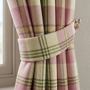 May include: Pink and cream plaid curtains with a matching tieback. The curtains have a woven texture and feature a pattern of pink, cream, yellow, and green squares. The tieback is cream with green stripes.