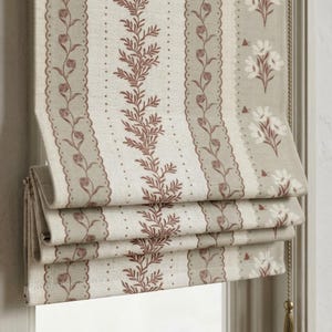 May include: A Roman blind with a floral and leaf pattern in beige, cream, and brown. The fabric has vertical stripes with alternating designs of flowers, leaves, and dotted lines. The blind is partially drawn, showing its layered construction.