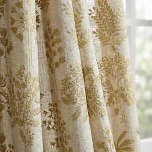 Könnte beinhalten: Beige und gold bestickte Gardinen. Die Gardinen zeigen ein sich wiederholendes Muster aus goldfarbenen botanischen Designs, darunter Blätter und Zweige, vor einem neutralen beigefarbenen Hintergrund. Der Stoff hat ein strukturiertes Aussehen.