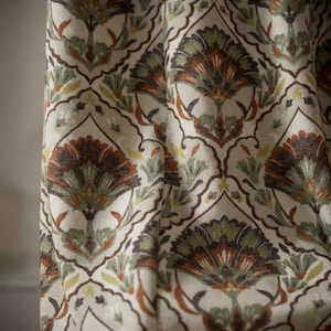 Könnte beinhalten: Cremefarbener Stoff mit einem sich wiederholenden Blumenmuster in Braun-, Grün- und Orangetönen. Das Design zeigt stilisierte Blumenformen und Blattmotive und erzeugt eine Vintage- oder Bohème-Ästhetik. Der Stoff scheint ein Vorhang- oder Gardinenmaterial zu sein.