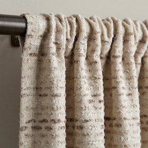 May include: Close-up of beige textured curtains hanging from a dark bronze curtain rail. The curtains have a woven appearance with subtle brown flecks, creating a neutral aesthetic. The fabric is gathered, adding depth and texture.