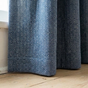 Puede incluir: Primer plano de cortinas estampadas en azul y blanco. La tela tiene un diseño de diamantes. Las cortinas cuelgan frente a una ventana y están hechas de un material grueso y texturizado. Las cortinas están sobre un piso de madera.