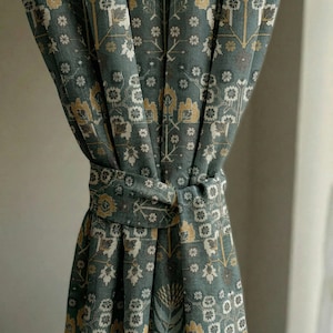 May include: Teal curtain with a repeating floral pattern in white and gold. The curtain is tied with a matching fabric tie. The design has a vintage or antique aesthetic, suitable for home decor.
